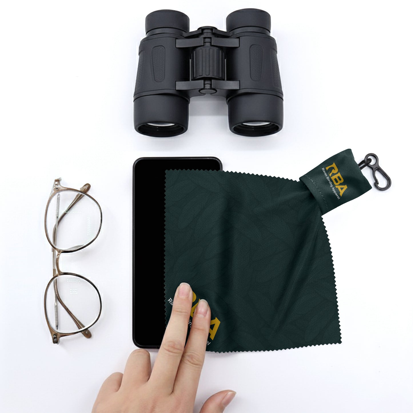 Microfiber lens cleaning cloth with a forest green feather pattern next to a pair of binoculars and a pair of glasses