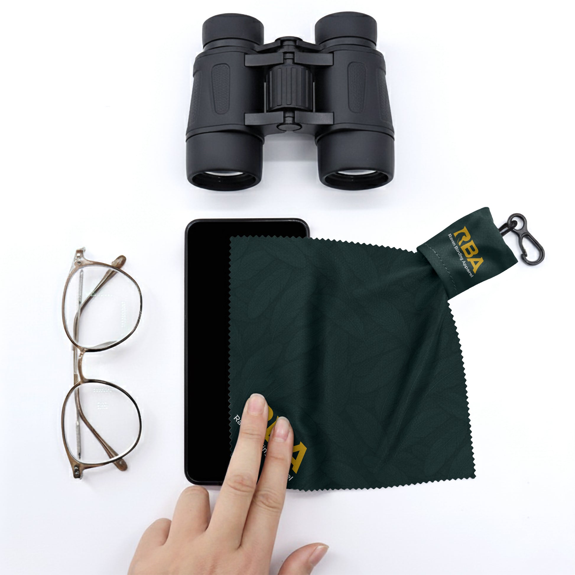 Microfiber lens cleaning cloth with a forest green feather pattern next to a pair of binoculars and a pair of glasses
