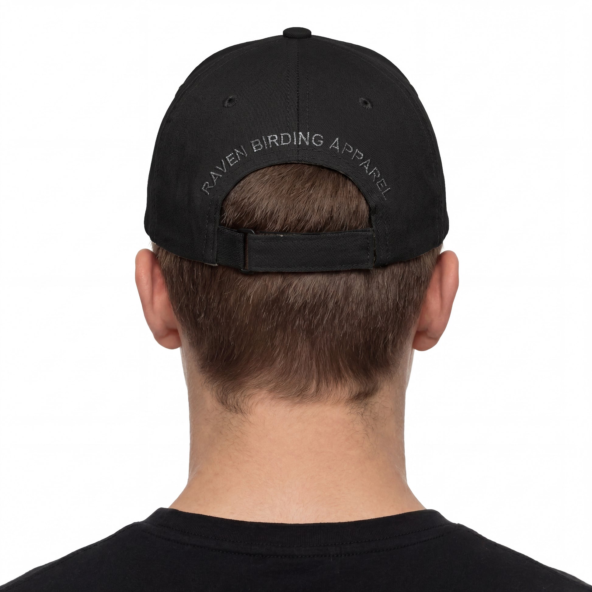 Person wearing a black cap with 'Raven Birding Apparel' branding on the back, on a white background.